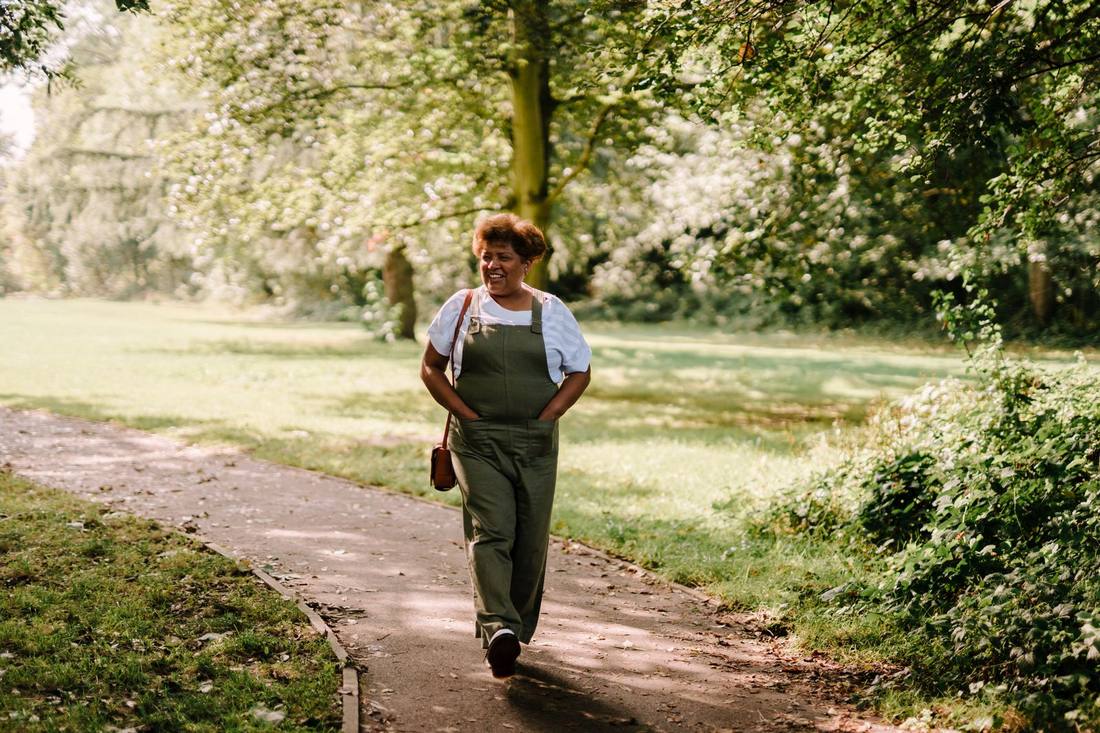 A smiling woman walking along a tree-lined path in a park
