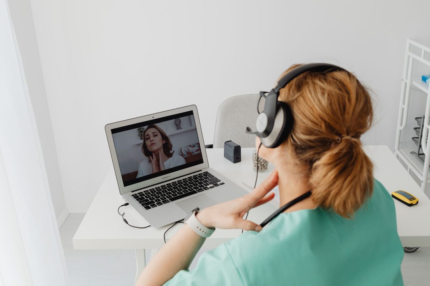 A clinician in scrubs and a headset holding a video visit with a patient on a laptop